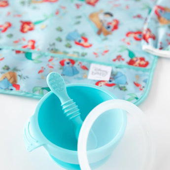 Bumkins Aqua feeding set on a character mat with the Sleeved Bib: Ariel for easy cleanup.