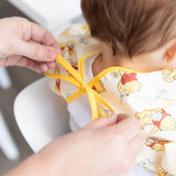 An adult uses the Bumkins Sleeved Bib: Winnie Loves Hunny, perfect for baby-led weaning, with waterproof fabric and cartoon bears.