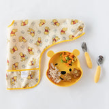 The Bumkins set includes a Winnie Loves Hunny sleeved bib and Pooh-shaped plate, ideal for baby-led weaning with waterproof fabric.