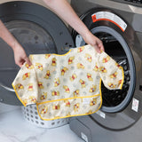 A person puts a Bumkins Sleeved Bib: Winnie Loves Hunny, made of waterproof fabric, into a front-loading washing machine.