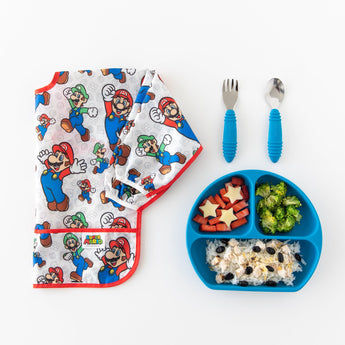 Kids meal with rice, broccoli, and stars comes with a spoon, fork, and a Bumkins Sleeved Bib: Super Mario™ Classic beside it.