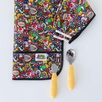 Super Mario™ Mashup Sleeved Bib and yellow-handled spoon & fork by Bumkins on a white background.