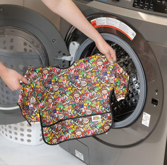 A person places a colorful Sleeved Bib: Super Mario™ Mashup by Bumkins into a front-load washer for more toddler adventures.