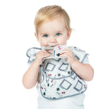 A blond baby finds teething relief with a Bumkins Silicone Teether: Game Boy™, wearing a matching patterned bib.