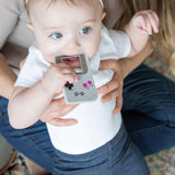 A seated adult holds the Bumkins Game Boy™ Silicone Teether as a baby chews, ensuring ultimate teething relief.