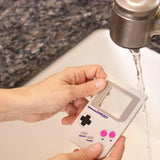 Hands washing a Bumkins Silicone Teether: Game Boy™ under a running faucet in the kitchen sink.