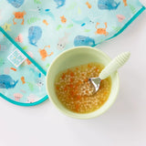 A bowl of baby soup with small pasta on Bumkins Junior Bib: Ocean Life featuring an adjustable sea-themed whales & crabs design.