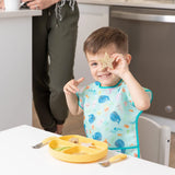 Child smiles holding a star-shaped bread, wearing a Bumkins Junior Bib in Ocean Life design with adjustable fit and waterproof fabric.