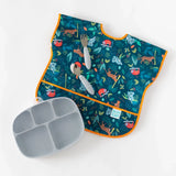 Bumkins Junior Bib: Jungle, forest animals print, orange edges, waterproof fabric. Includes gray plate/utensils. Adjustable white background.