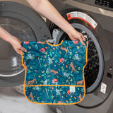 Someone places a waterproof Bumkins Junior Bib: Jungle, with animal patterns, into a front-loading washing machine.