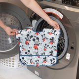 Placing a Bumkins Junior Bib: Mickey Mouse Classic into the washer, with a laundry basket nearby.