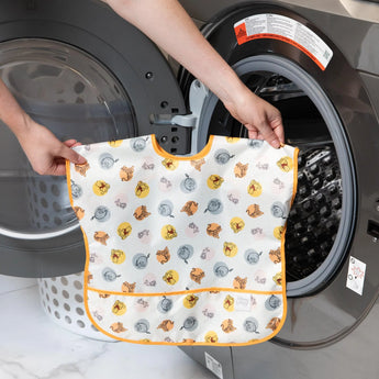 Someone loading a Bumkins Junior Bib: Winnie and Friends into a front-loading washing machine.