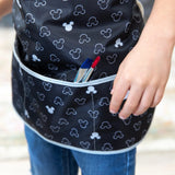 Child in Bumkins Mickey Mouse Icon B+W smock with waterproof fabric and adjustable waist, pairing blue jeans, paintbrushes in pocket.