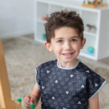 A child smiles, painting in a Bumkins Short-Sleeved Smock with Mickey Mouse Icon B+W; toys and books fill the shelves behind.