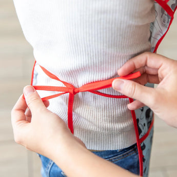 Tying a red apron bow around a white shirt and jeans, just like wearing the Bumkins Short-Sleeved Smock: Mickey Mouse Classic.