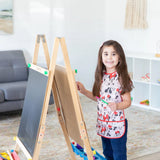 A child painting at an easel in the living room, wearing a Bumkins Short-Sleeved Minnie Mouse Classic Smock and holding a paintbrush.