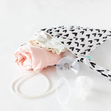 A baby care kit with a pink blanket, white clothes, and Bumkins Wet Bag: Hearts in waterproof fabric.