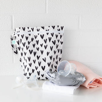 Bumkins Wet Bag: Hearts, baby bottle parts, and pink cloth diaper on a white surface.