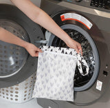 A person places a Bumkins Wet Bag: Hearts into a front-loading washing machine.