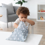 A child with curly hair opens a Bumkins Wet Bag: Arrow on a white table in a modern, cozy living room.