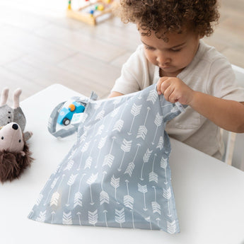 A child at a table opens a Bumkins Wet Bag: Arrow, revealing a toy hedgehog and another item.