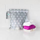 Bumkins Wet Bag: Arrow in waterproof fabric next to cloth diapers and nursing gear on a white surface against a white brick wall.