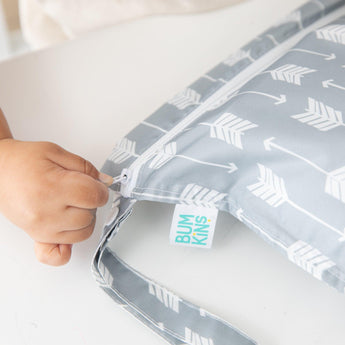 A child zips a Bumkins Wet Bag: Arrow, a gray reusable bag with white arrows.