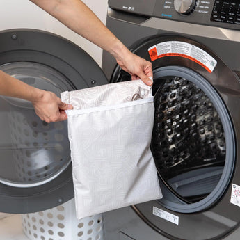 Person loading a Bumkins Wet Bag: Wander into a front-load washer with a laundry basket by the side.