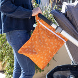 Attach the Bumkins Wet Bag: Grounded, a stylish orange waterproof accessory, to your stroller handle for outdoor convenience.