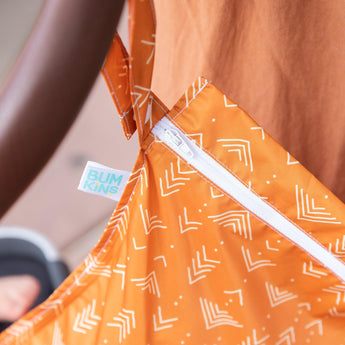 Close-up of the Grounded wet bag by Bumkins, featuring a white geometric pattern on orange, with waterproof fabric and visible zipper.