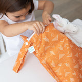 A child opens the Bumkins Wet Bag: Grounded, featuring vibrant waterproof fabric and white geometric designs, next to a stuffed unicorn.