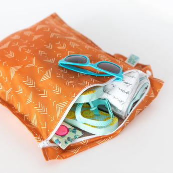 Partially open Wet Bag: Grounded by Bumkins in an orange pattern with sunglasses, a rolled-up cloth, and various small items inside.