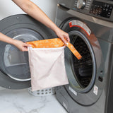 A person places a Bumkins Wet Bag: Grounded, a stylish waterproof bag, into a front-loading washing machine.