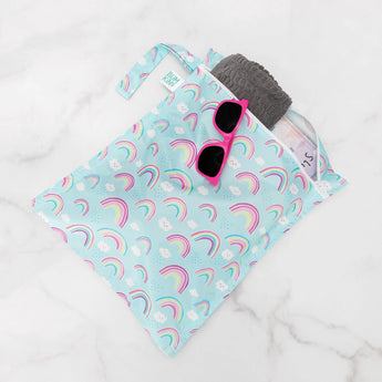 The Bumkins Wet Bag: Rainbows holds a gray towel and pink sunglasses on white marble.