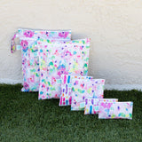 Six Bumkins Wet Bags: Watercolor with floral patterns on grass, in front of a cream-colored wall; made from waterproof fabric.