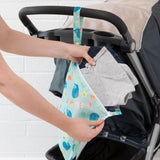 Hands placing clothes into the colorful Bumkins Wet Bag: Ocean Life attached to a stroller handle.