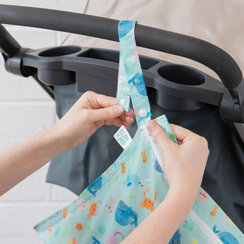 Attaching a Bumkins Wet Bag: Ocean Life, with bright animal patterns and waterproof fabric, to a stroller handle.