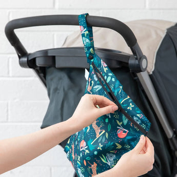 Hands unzipping a Bumkins Wet Bag: Jungle, attached to a stroller handle.