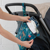 Person places clothes into a Bumkins Wet Bag: Jungle, made of waterproof fabric, attached to a stroller handle.