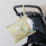 A stroller with a Bumkins Camp Gear Wet Bag, filled with a white shirt and denim shorts, adorned with baby-themed illustrations.