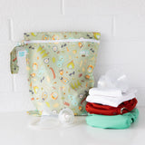 A Bumkins Camp Gear wet/dry bag with waterproof fabric is placed next to cloth diapers and breast pump parts, ideal for travel.