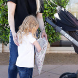 A child peeks into a Bumkins Wet Bag: Floral, made of waterproof fabric, held by an adult next to a stroller outdoors.