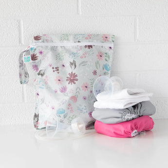 A Bumkins Wet Bag: Floral, made from waterproof fabric, rests next to colorful cloth diapers and cup lids on a white surface.