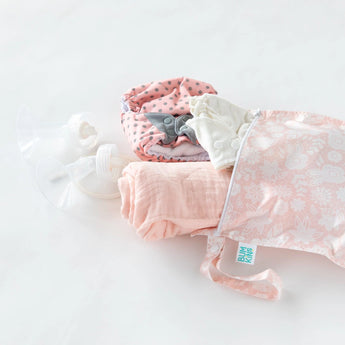 Bumkins essentials like a pink cloth diaper and bottle parts are in a floral Wet Bag: Lace made of waterproof fabric.