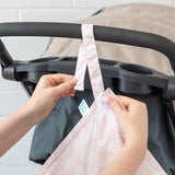 Attaching the Lace Wet Bag by Bumkins, a floral waterproof pink cover, to a stroller with buttoned straps.