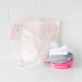 Bumkins Lace Wet Bag, waterproof, with three reusable cloth diapers (white, gray, pink) and feeding pump accessories on a white surface.