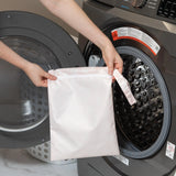 A person places a Bumkins Wet Bag: Lace into a front-loading washing machine.