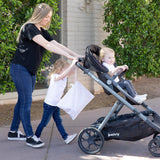 A woman strolls with a toddler in a stroller, aided by another, essentials packed in a Bumkins Wet Bag: Lace amidst the greenery.