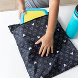 A child places a yellow container in a Bumkins Wet Bag: Mickey Mouse Icon Black + White next to a blue water bottle.