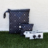 Four Mickey Mouse Icon Black + White wet bags by Bumkins placed on grass against a white wall.